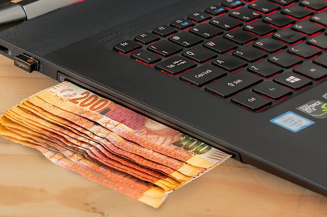 Dinero sentado al lado de la computadora portátil en la mesa.
